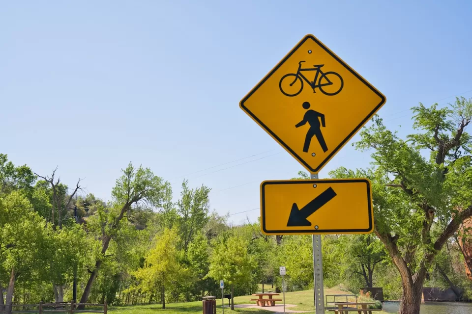 A yellow sign points to a bike and pedestrian path with open park space in the background.